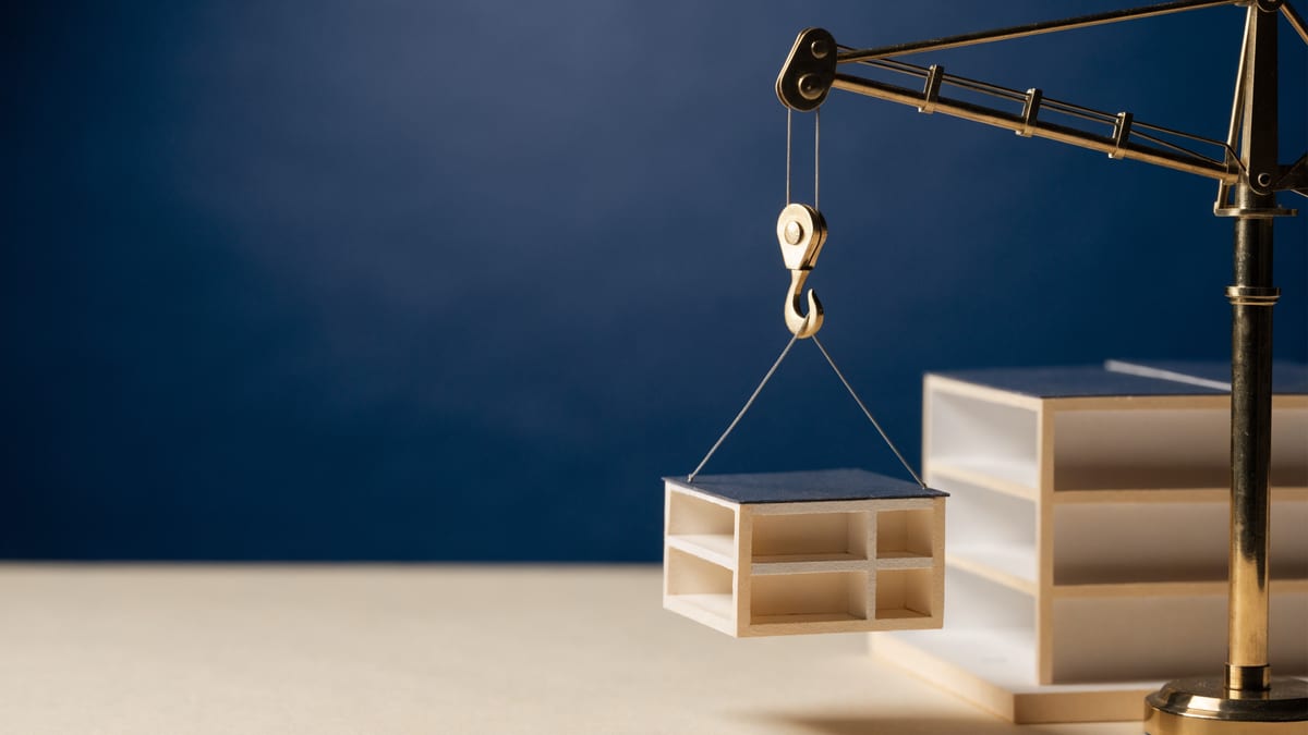 Scale model of a modular home section on a navy backdrop with a small brass crane, representing factory stage funding