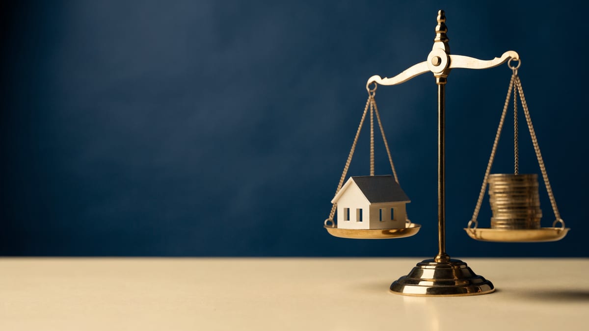 Scale model house beside a set of brass balance scales on a navy backdrop, representing debt to income limits